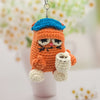 Crocheted cat keychain with a blue hat and white paws on a blurred floral background