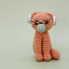 Crocheted pink cat toy with closed eyes and white ears on a light green background