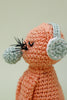 Crocheted rabbit toy with green mittens and headband on a light background