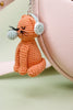 Crocheted orange cat keychain with white paw pads attached to a pink bag.